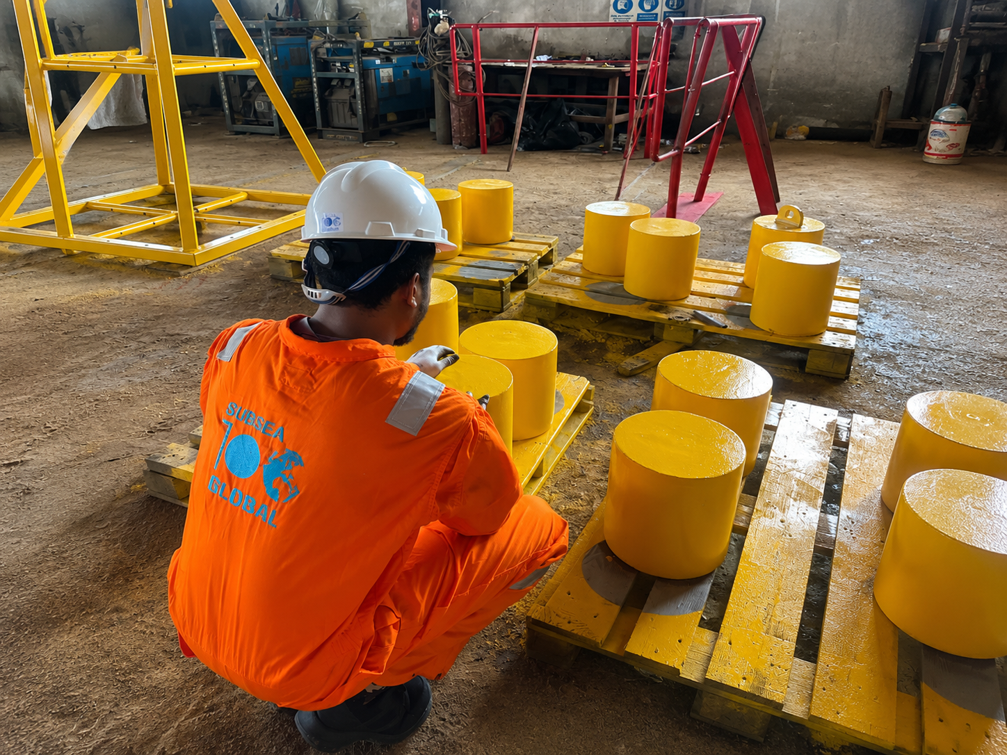 Subsea100 technician preparing yellow subsea buoyancy modules on pallets in the workshop